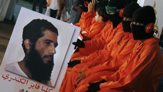 Protesters dressed in  orange prison outfits and  black masks attend a demonstration outside the US embassy in Kuwait City on May 2, 2012, calling for the release of Kuwaiti prisoners still behind the bars at the US detention camp in Guantanamo Bay. Fawzi al-Odah and Fayez al-Kandari (portrait) are the only two Kuwaitis still held at the US prison. AFP PHOTO / YASSER AL-ZAYYAT        (Photo credit should read YASSER AL-ZAYYAT/AFP/GettyImages)